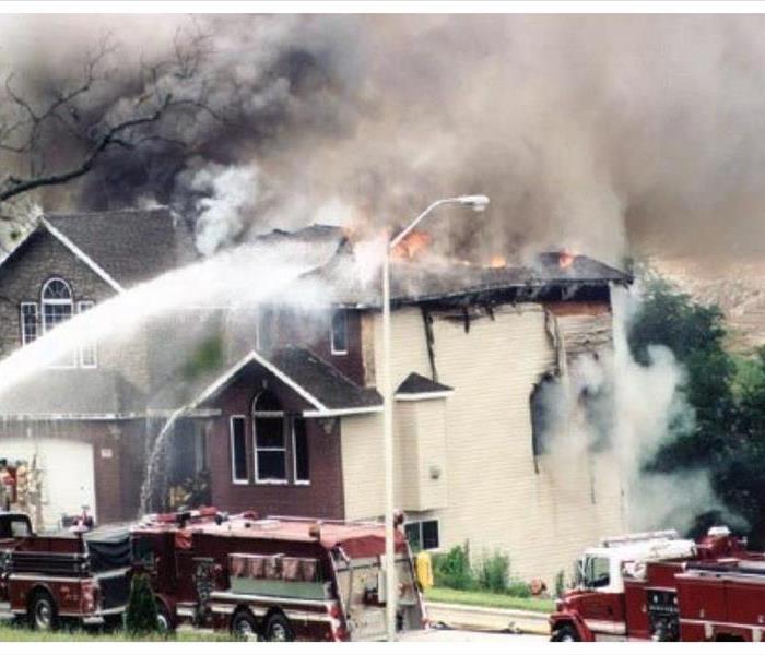 Exterior photo of a home on fire being handled by fire department.