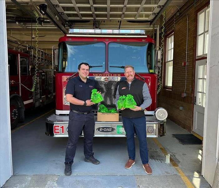 Two men standing in front of fire engine each holding a green bag.